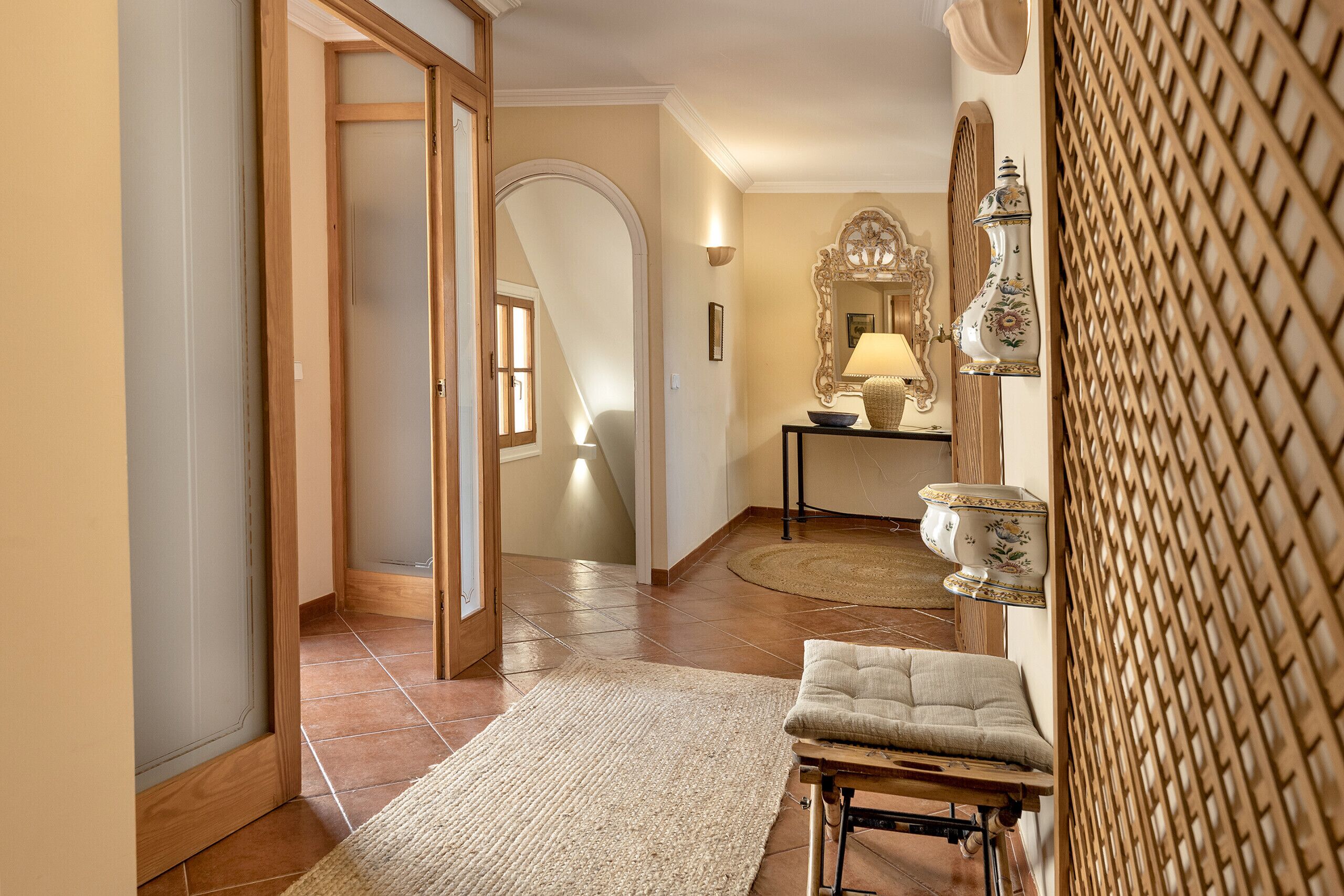A hallway with a wooden door, a rug, a bench, a lamp, and a decorative mirror.