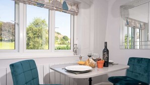A dining area with a table set for two, two teal chairs, a bottle of wine, a glass, and a bowl of fruit. - Kentmere Haven with Parking by LetMeStay (Kendal)