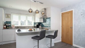 A modern kitchen with a central island, two bar stools, a wooden door, and a decorative wall piece. - Kentmere Haven with Parking by LetMeStay (Kendal)