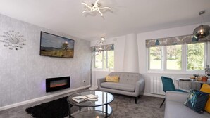 A modern living room with a fireplace, a sofa, a coffee table, and a large window with a view of the outdoors. - Kentmere Haven with Parking by LetMeStay (Kendal)