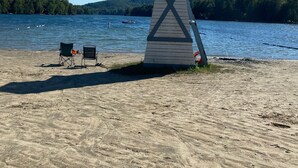 A beach with a lifeguard tower, two folding chairs, and a small boat on the water. - Lakehouse w/ stunning views and a swimming pool‼️ (Val-des-Bois)
