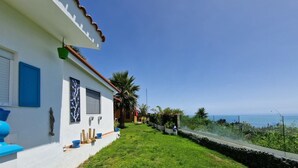 A coastal property with a white exterior, blue accents, a well-maintained lawn, and a view of the sea.