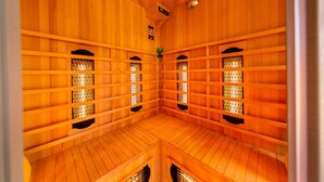 A sauna room with wooden walls and floors, featuring multiple benches and ventilation grills.