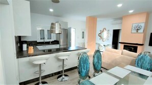 A modern kitchen with white cabinets, a central island with bar stools, and a dining area with a glass table and chairs.