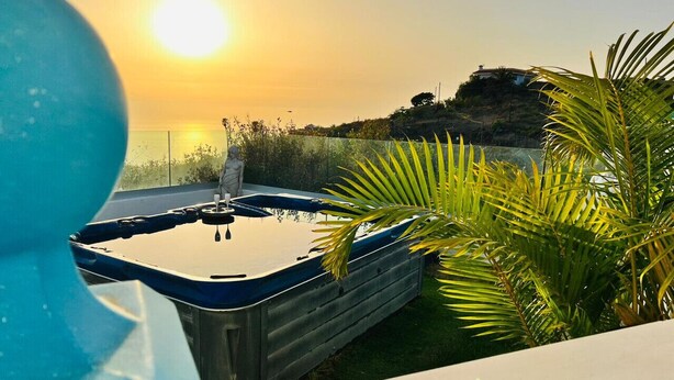 A swimming pool with a hot tub, surrounded by palm trees and a view of the sunset.