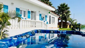 A swimming pool with hot tubs in front of a white building with blue shutters.