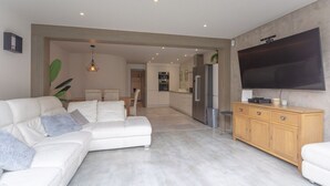 A modern living room with a white sofa, a wooden cabinet, and a flat-screen TV mounted on the wall.