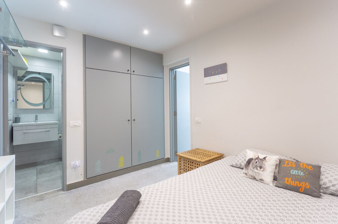A bedroom with a bed, a wardrobe, a small table, and a wall-mounted shelf.