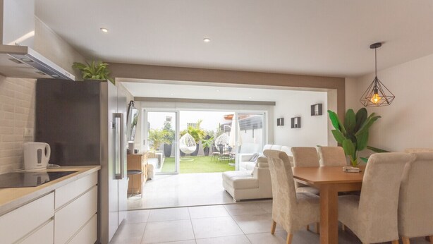 A modern kitchen with a dining area, a large sliding glass door leading to a patio, and a hanging light fixture.