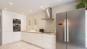 A modern kitchen with white cabinets, stainless steel appliances, a built-in oven, a range hood, and a refrigerator.