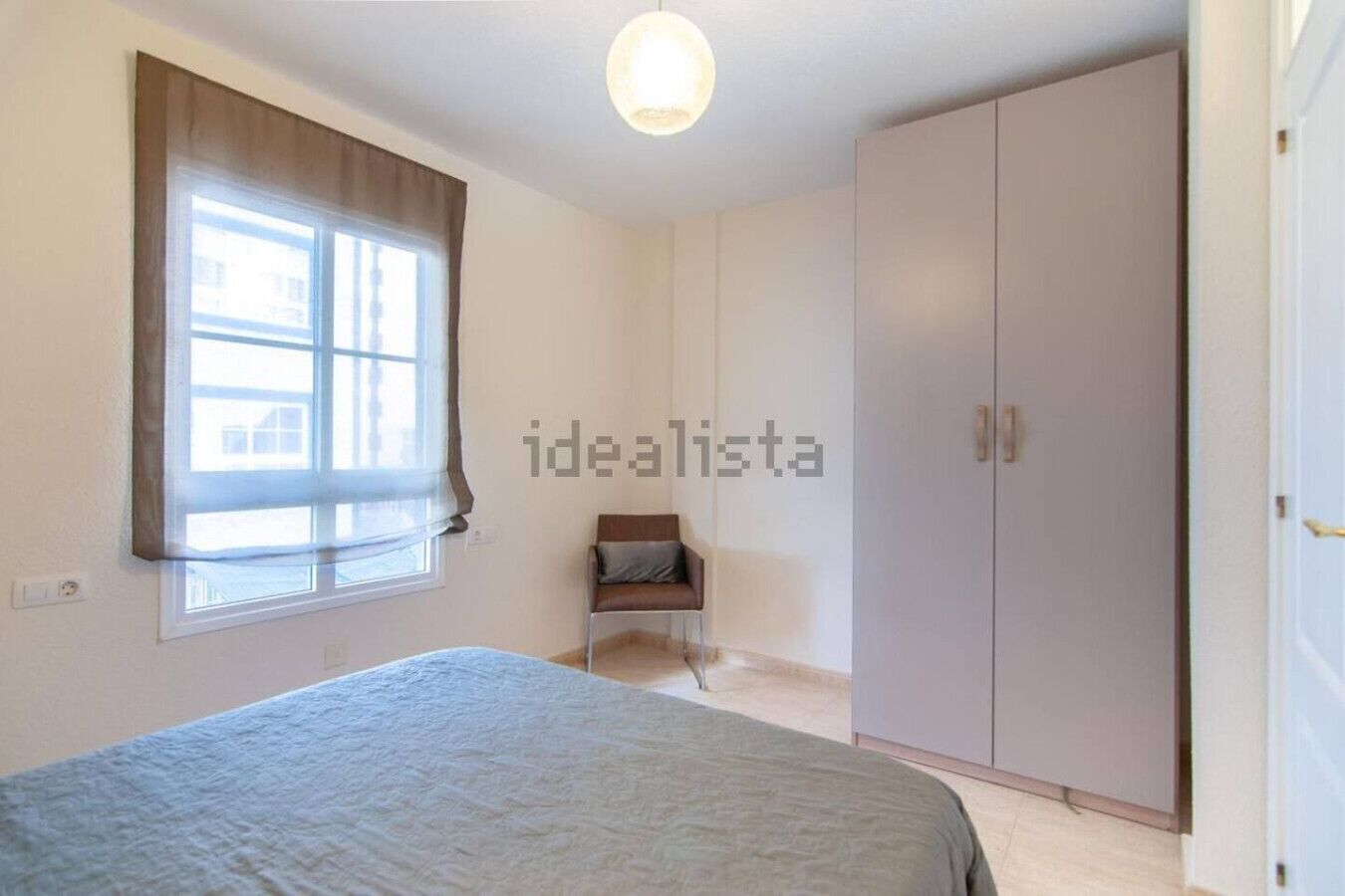 Une chambre à coucher avec un lit, une armoire, une chaise et une fenêtre avec des rideaux.