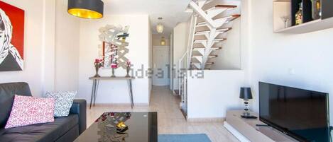 A modern living room with a sofa, coffee table, TV, and a staircase leading to another level.