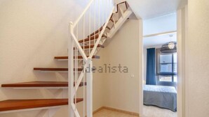 Un escalier avec des marches en bois et une rampe blanche menant à une chambre à coucher où se trouvent un lit et une fenêtre.