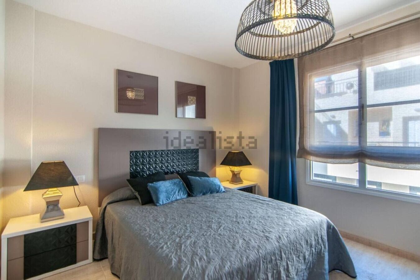 A modern bedroom with a large bed, two bedside lamps, a decorative headboard, and a view of the outside through a window.
