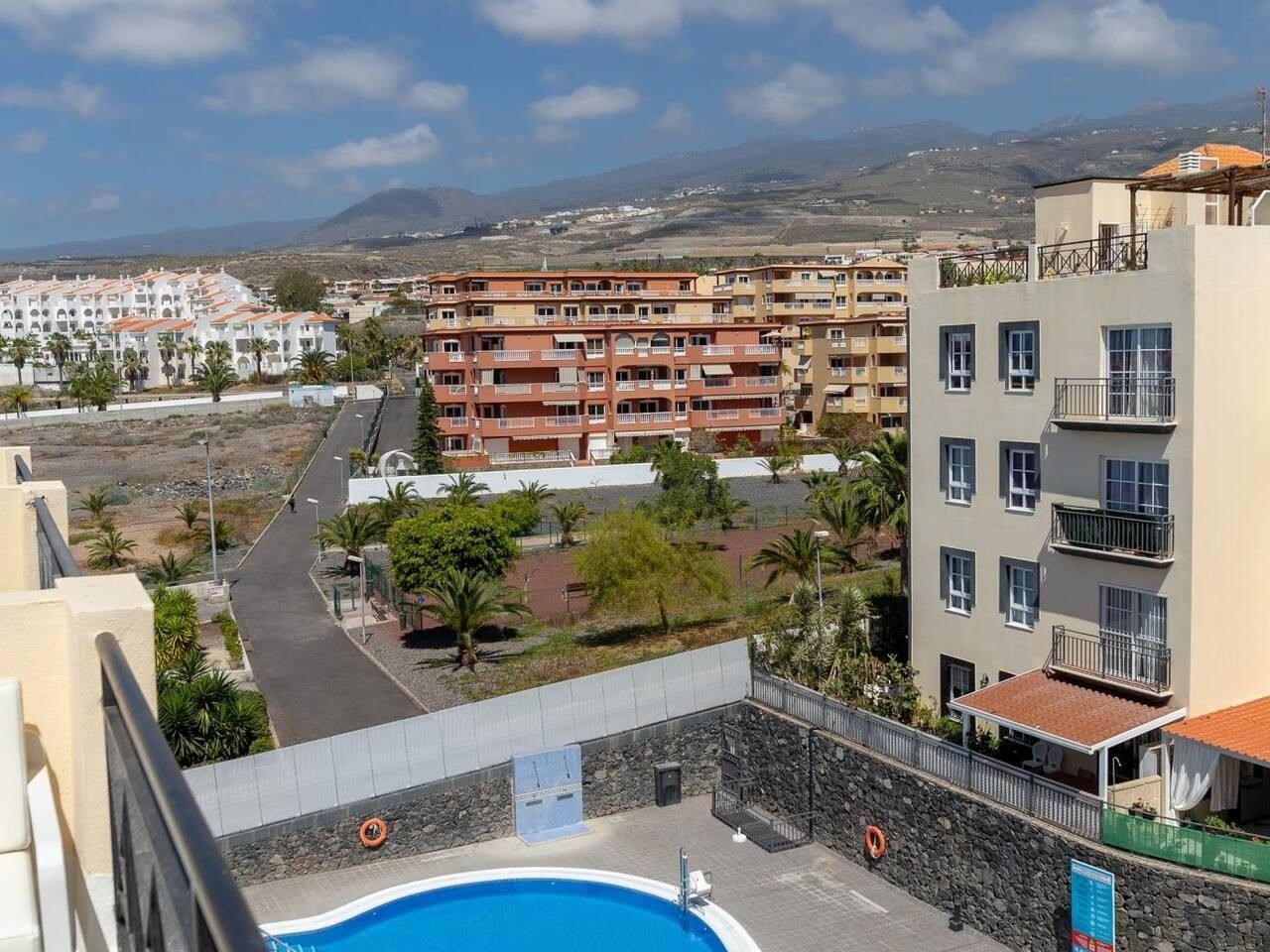 A residential building with multiple balconies, a swimming pool, and a view of the surrounding landscape.