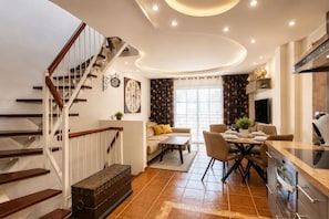 Eine moderne Küche mit einer zentralen Kochinsel, einem Essbereich mit einer Couch und Sesseln sowie einer Treppe mit Holzwangen.