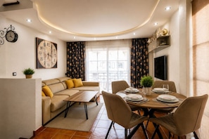 A modern living room with a sofa, a dining table set for four, and a large wall clock. - Aqua Vista 2 bed Penthouse with great views (Callao Salvaje)