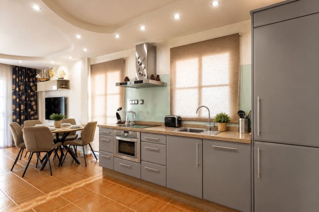 A modern kitchen with grey cabinets, a built-in oven, and a dining area with a table and chairs.
