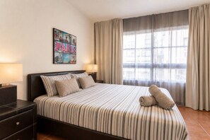 A hotel room with a large bed, two bedside tables, a wall-mounted artwork, and a window with curtains.