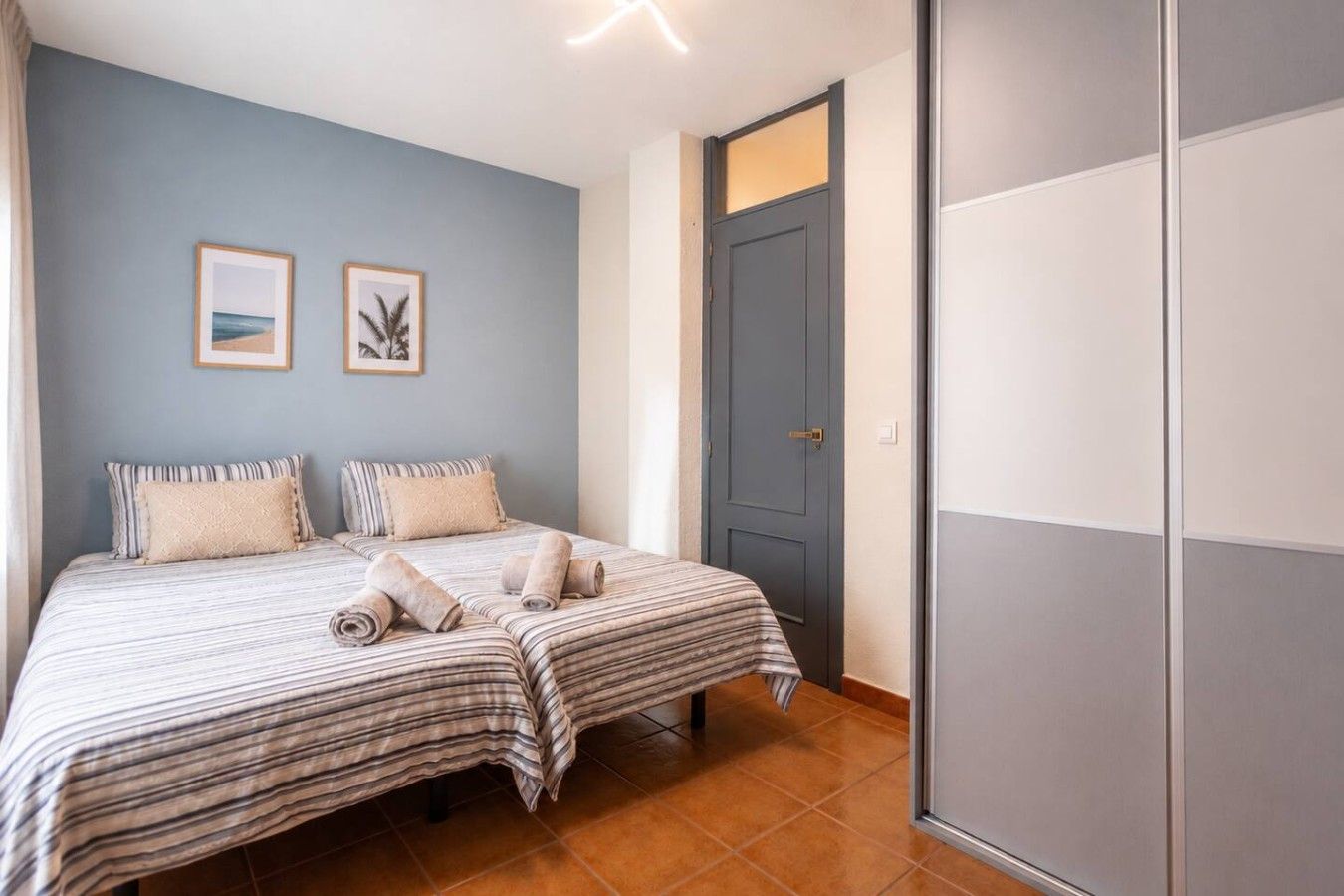 A bedroom with two beds, a door, and two framed pictures on the wall.