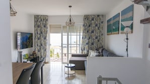 Un salon moderne avec un canapé, une table à manger et un téléviseur. Il y a des rideaux et un tableau au mur.