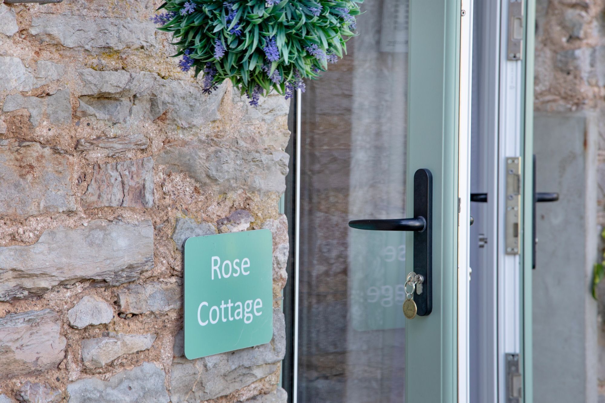 A stone wall with a sign reading "Rose Cottage" and a door with a key in the lock.