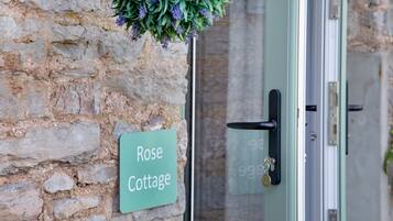 A stone wall with a sign reading "Rose Cottage" and a door with a key in the lock.