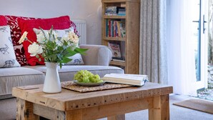 A cozy living room with a wooden coffee table, a vase of flowers, and a bookshelf in the background. - Rose Cottage in Marldon, Paignton, Devon (Paignton)