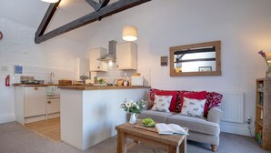 A modern kitchen with white cabinets, a central island, and a wooden bench with a book and flowers. - Rose Cottage in Marldon, Paignton, Devon (Paignton)