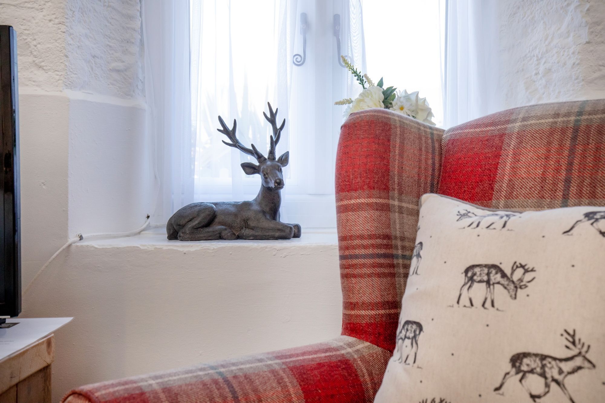A cozy room with a red plaid sofa, a decorative deer statue on a windowsill, and a wall-mounted TV.