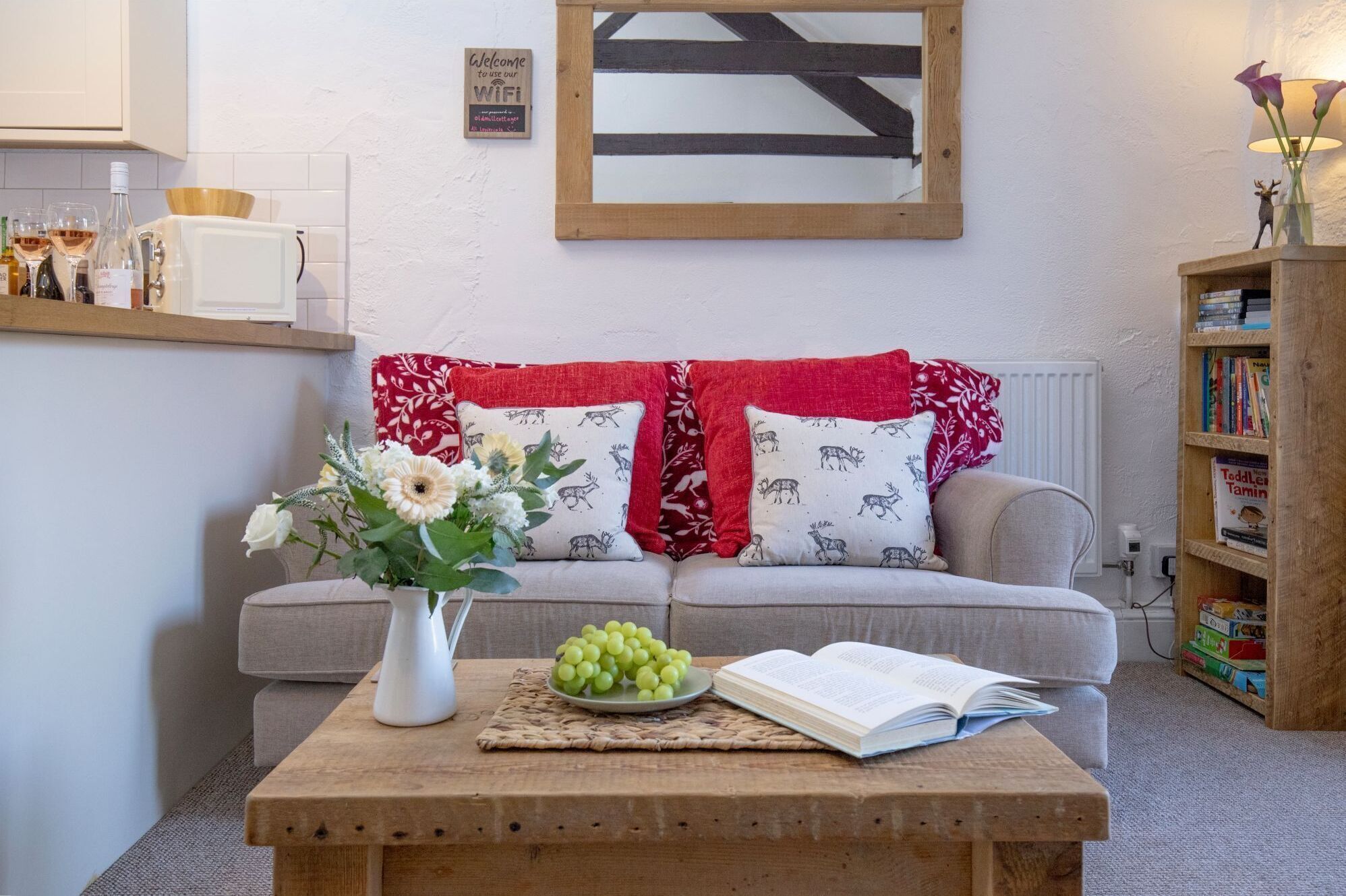 A cozy living room with a sofa, a coffee table with a book, a vase of flowers, and a bookshelf.