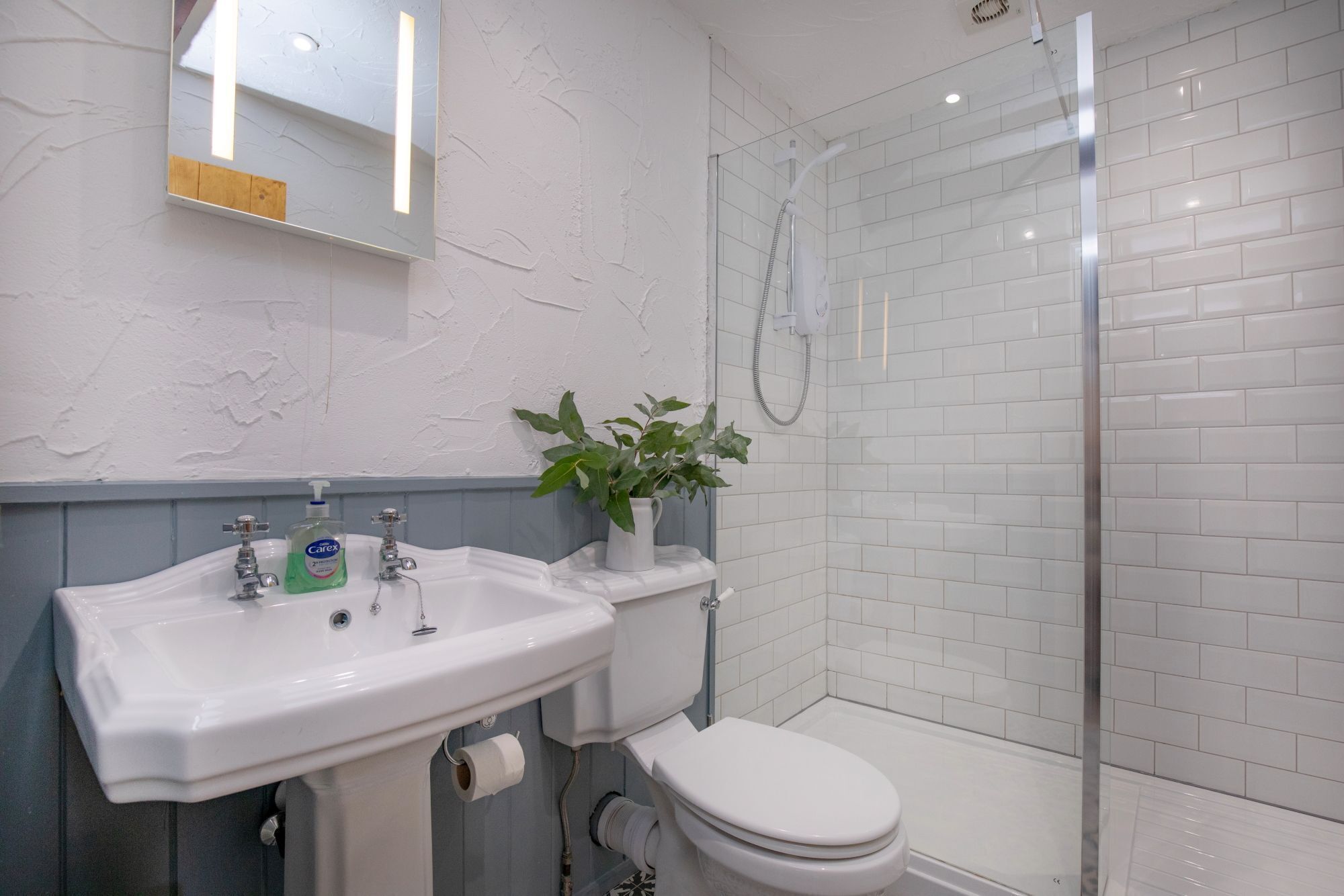 A bathroom with a white sink, toilet, and glass-enclosed shower.