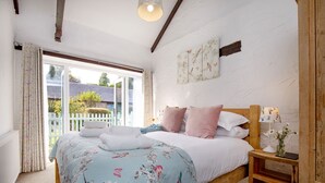 Une chambre à coucher avec un lit, une table de chevet avec une lampe, une fenêtre avec des rideaux et un mur orné d’un tableau représentant des motifs floraux.