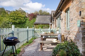 A stone cottage with a wooden table and a barbecue grill in the garden. - Daisy Cottage - Sleeps 4 guests in 2 bedrooms (Paignton)