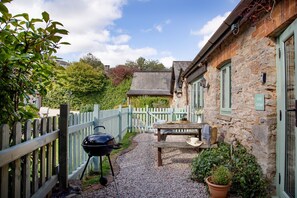 A stone cottage with a gravel patio, a barbecue, and a wooden table with outdoor seating. - Daisy Cottage - Sleeps 4 guests in 2 bedrooms (Paignton)