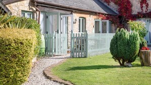 Une charmante maison en pierre avec une clôture en bois peinte en blanc, une pelouse bien entretenue et un petit arbre au premier plan.