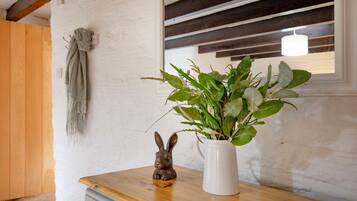 Una mesa de madera con un jarrón blanco que contiene plantas verdes y una pequeña figurina de conejo.