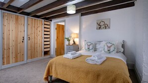 Een slaapkamer met een bed, een houten kledingkast, een nachtkastje met een lamp en een schilderij aan de muur.