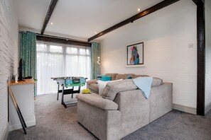 A cozy living room with a sofa, a foosball table, and a window with curtains.