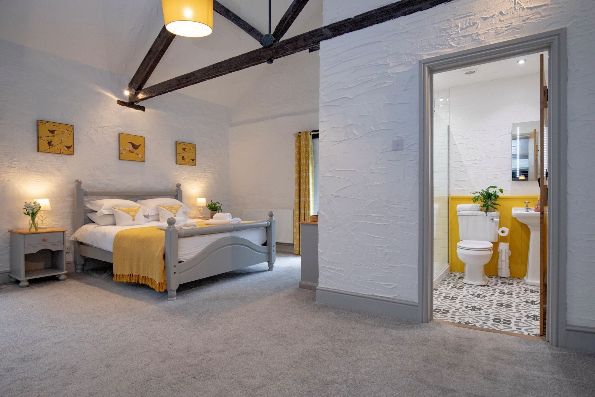 Un dormitorio con cama, mesitas de noche y un velador. Se ve un baño por una puerta abierta.