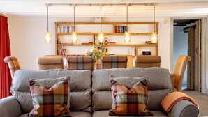 Een gezellige woonkamer met een grijze bank, geruite kussens en een houten boekenplank vol boeken.