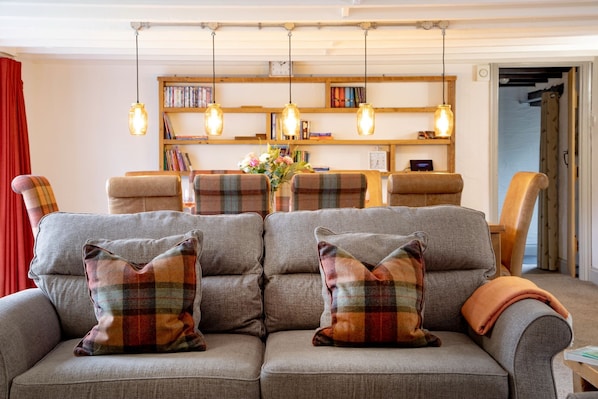 A cozy living room with a grey sofa, plaid cushions, and a wooden bookshelf filled with books.