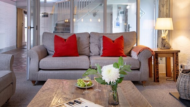 Een moderne woonkamer met een grijze bank, rode kussens, een houten salontafel en een witte bloevas.
