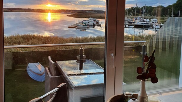 A room with a large window overlooking a marina and sunset. - Modern vacation apartment with balcony directly on the Peene (Ziemitz)