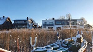 A modern house with a large garden, a wooden boat with snow-covered parts, and a clear blue sky. - Modern vacation apartment with balcony directly on the Peene (Ziemitz)