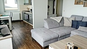 A modern living room with a grey sofa, a wooden coffee table, and a kitchen area with a stove and cabinets. - Modern vacation apartment with balcony directly on the Peene (Ziemitz)