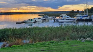 A marina with boats docked, surrounded by grassy areas and a calm body of water reflecting the sky. - Modern vacation apartment with balcony directly on the Peene (Ziemitz)