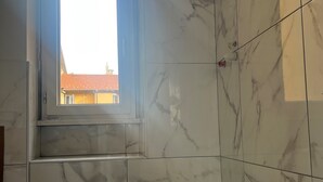 Un baño con azulejos de mármol, una ventana y vistas de edificios.