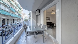 En balkon med spisebord og stole, med udsigt over en travl gade med parkerede biler og bygninger.