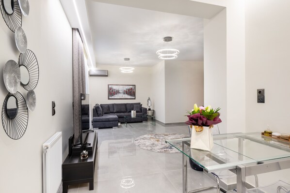 A modern living room with a glass coffee table, a dark sofa, and a painting on the wall.